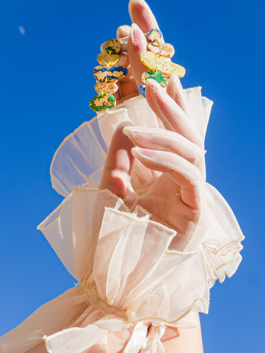 Hands holding Love Hand and Heart earrings. Wearing vintage gloves.