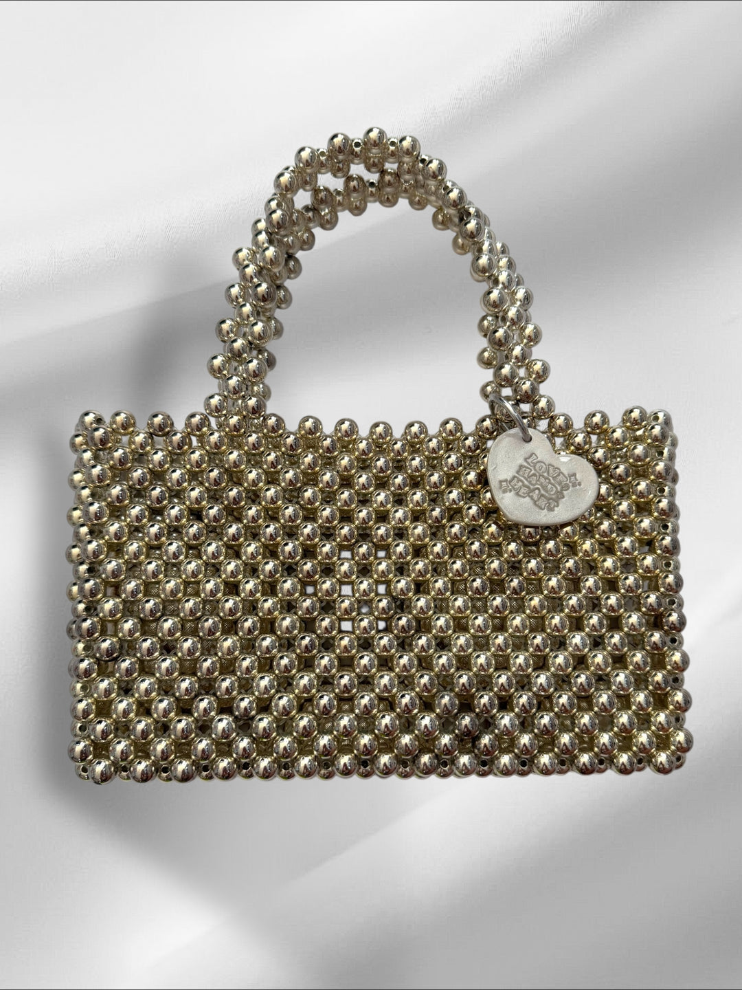 Silver beaded handbag with a heart-shaped tag on a white background