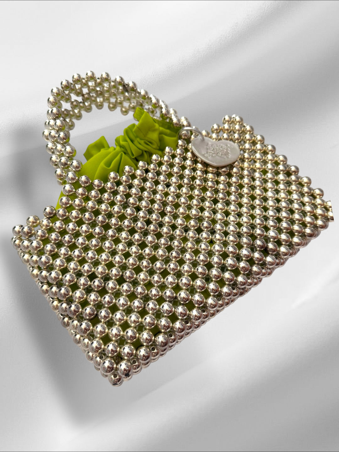 Silver beaded handbag with a green pouch on a white background