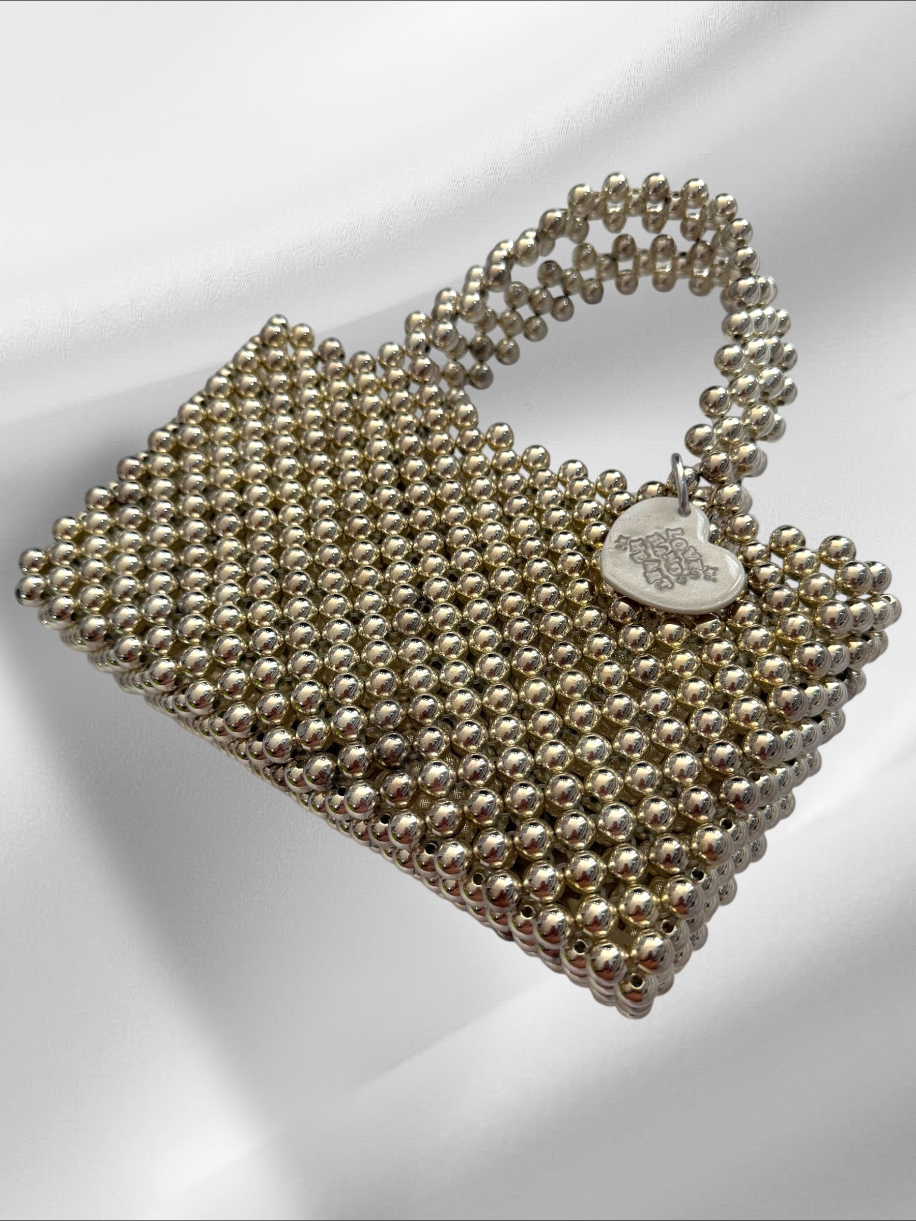 Silver beaded handbag with a heart charm on a white background