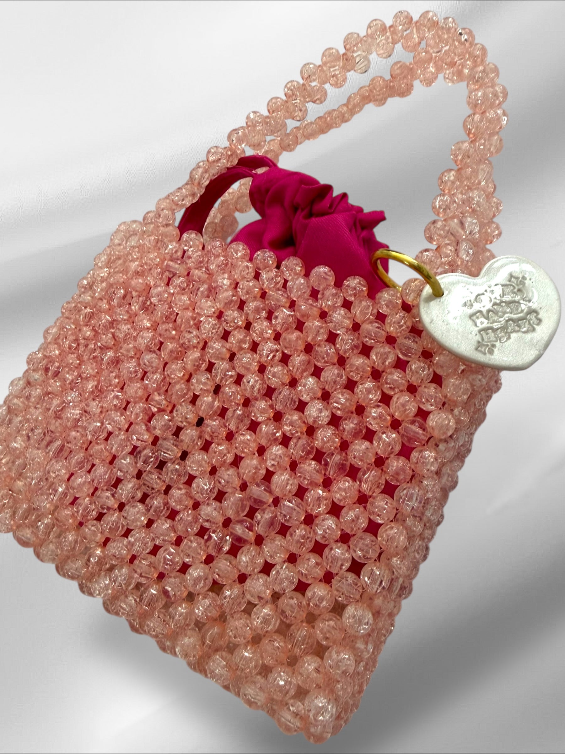 Pink beaded handbag with a red drawstring on a light gray background