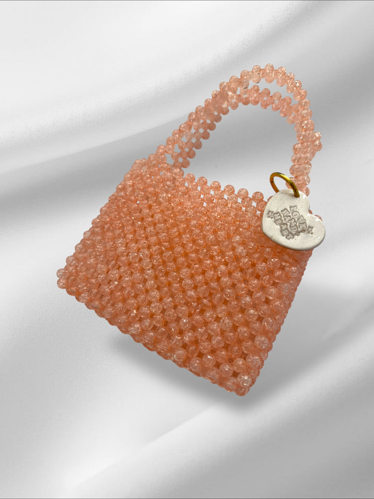 Pink beaded handbag with a heart-shaped tag on a light gray background