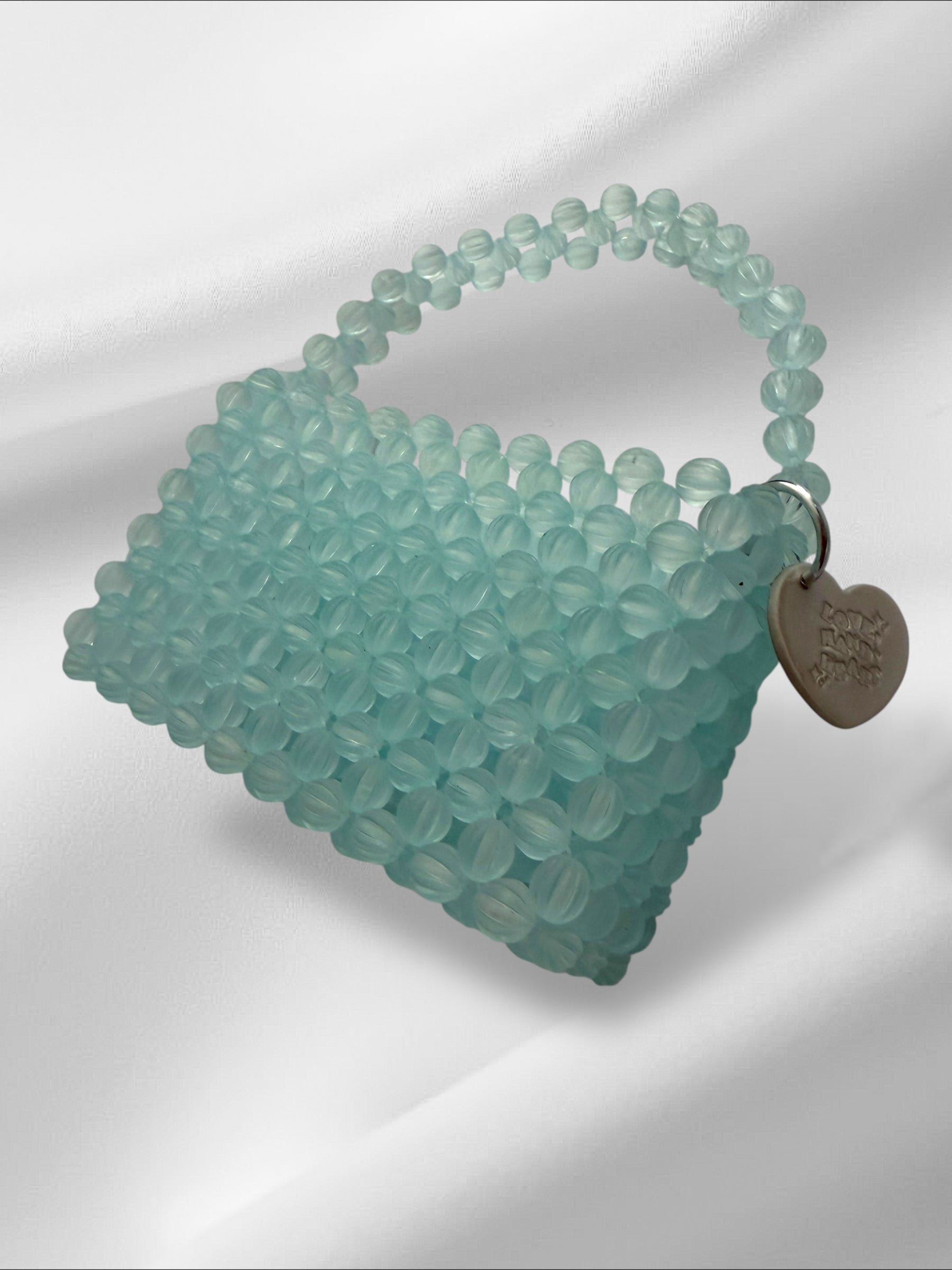 Teal beaded handbag with a heart-shaped tag on a light gray background