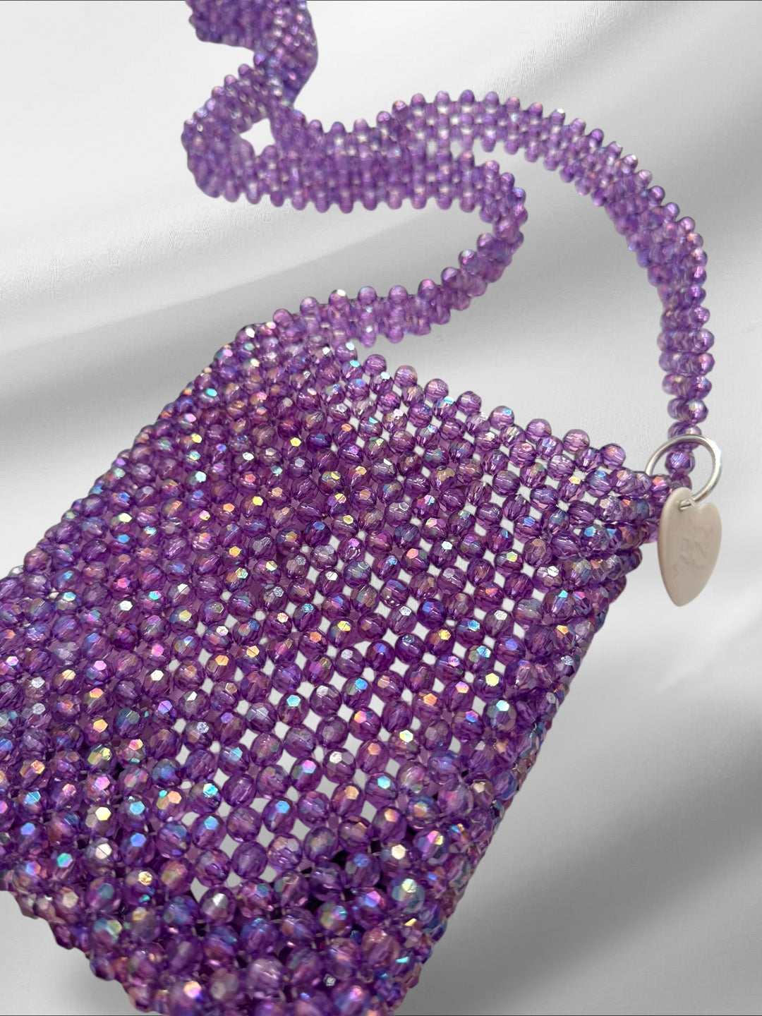 Purple beaded crossbody bag with a hand beaded strap on a light gray background