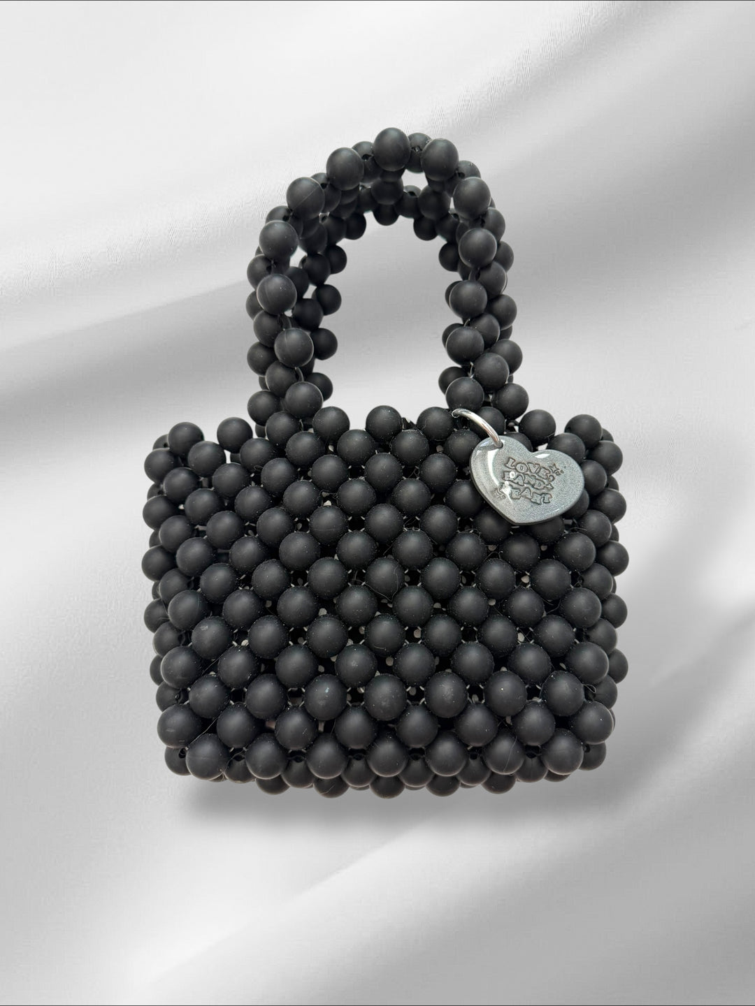 Black beaded handbag with a heart-shaped tag on a white background