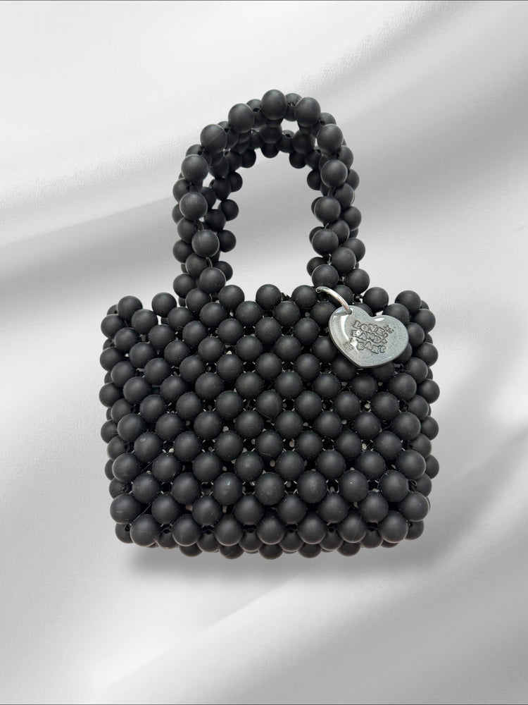 Black beaded handbag with a heart-shaped tag on a white background