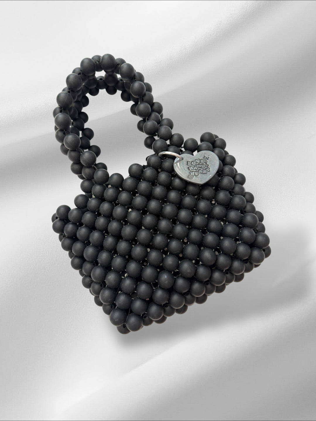 Black beaded handbag with a heart-shaped tag on a white background