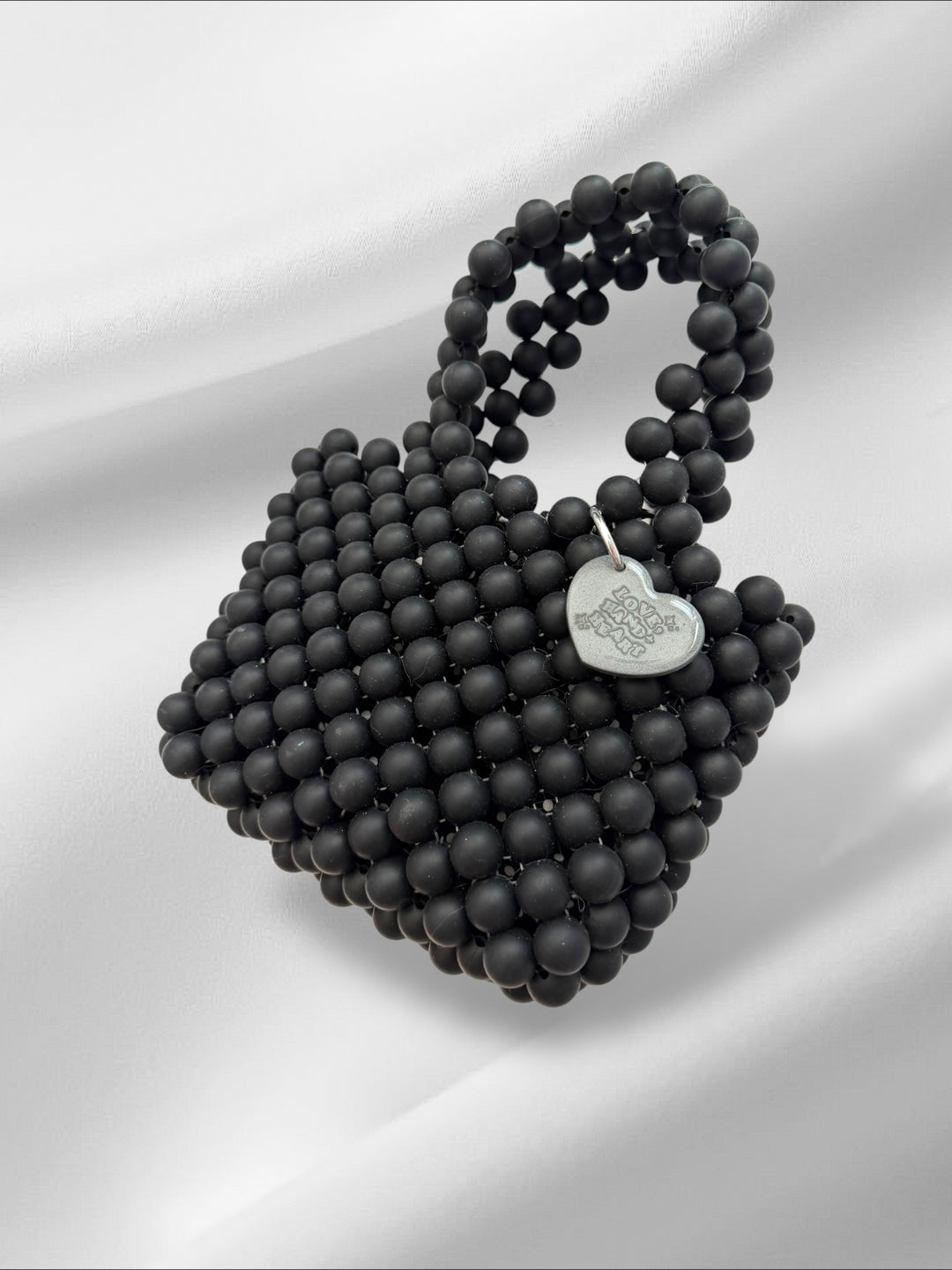 Black beaded handbag with a heart-shaped logo on a white background
