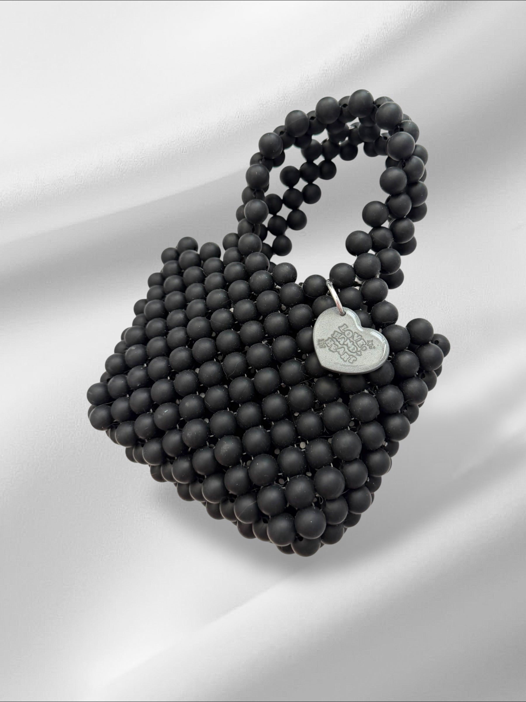 Black beaded handbag with a heart-shaped logo on a white background