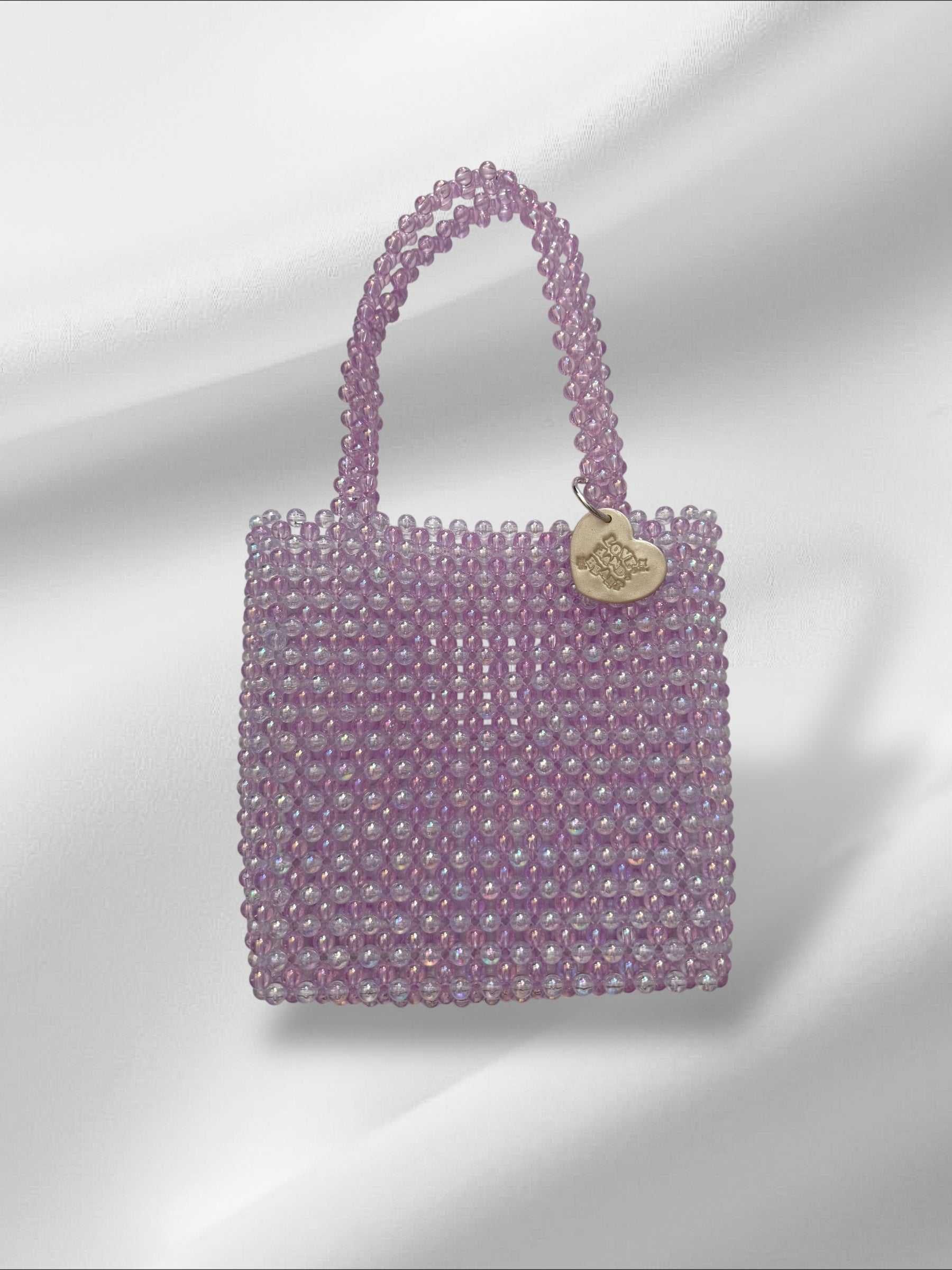 Purple beaded handbag with a heart-shaped tag on a light gray background
