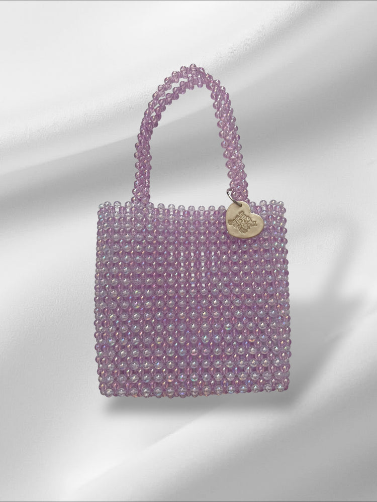 Purple beaded handbag with a heart-shaped tag on a light gray background