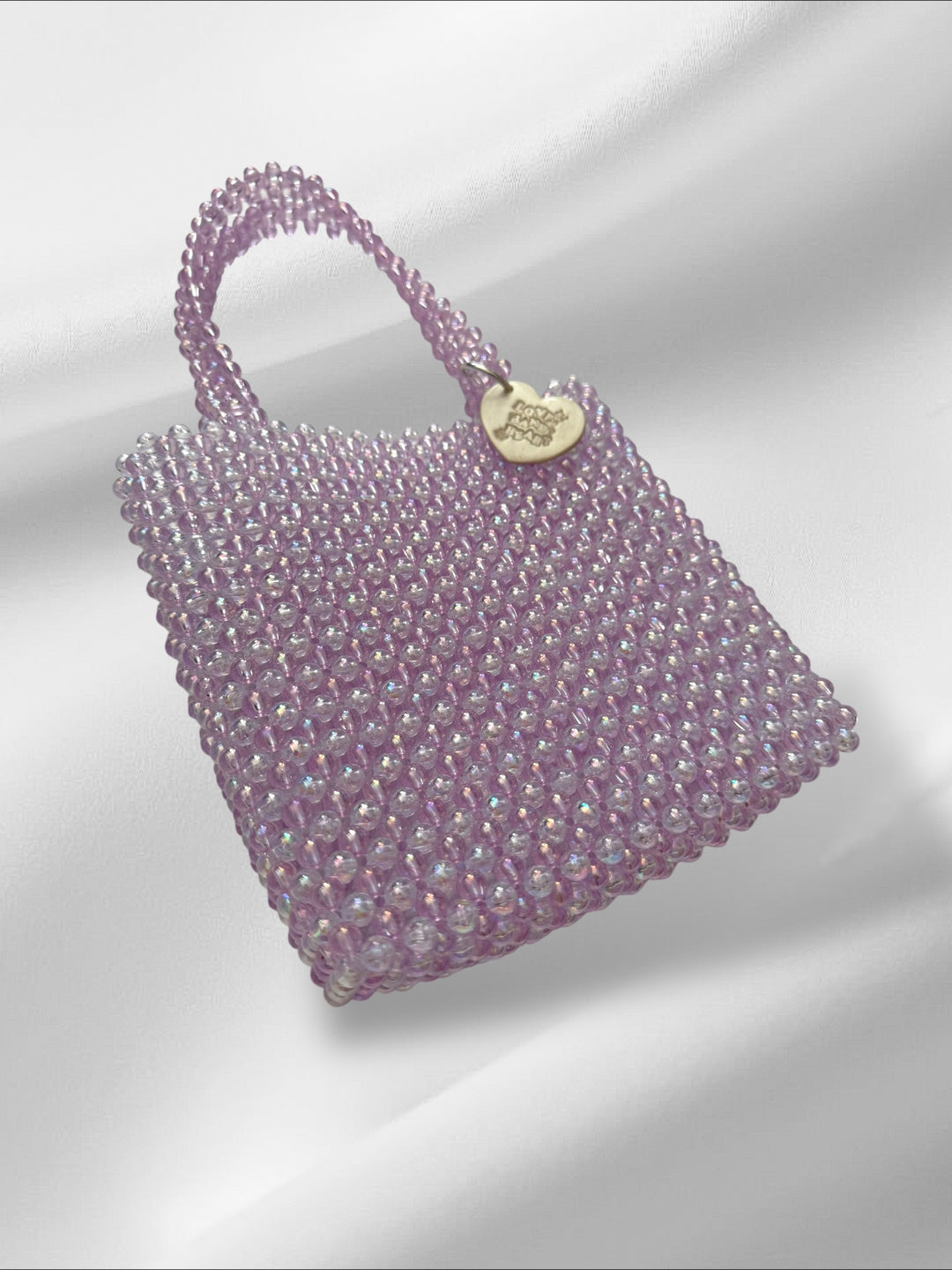 Purple beaded handbag with a white metallic clay tag on a light gray background