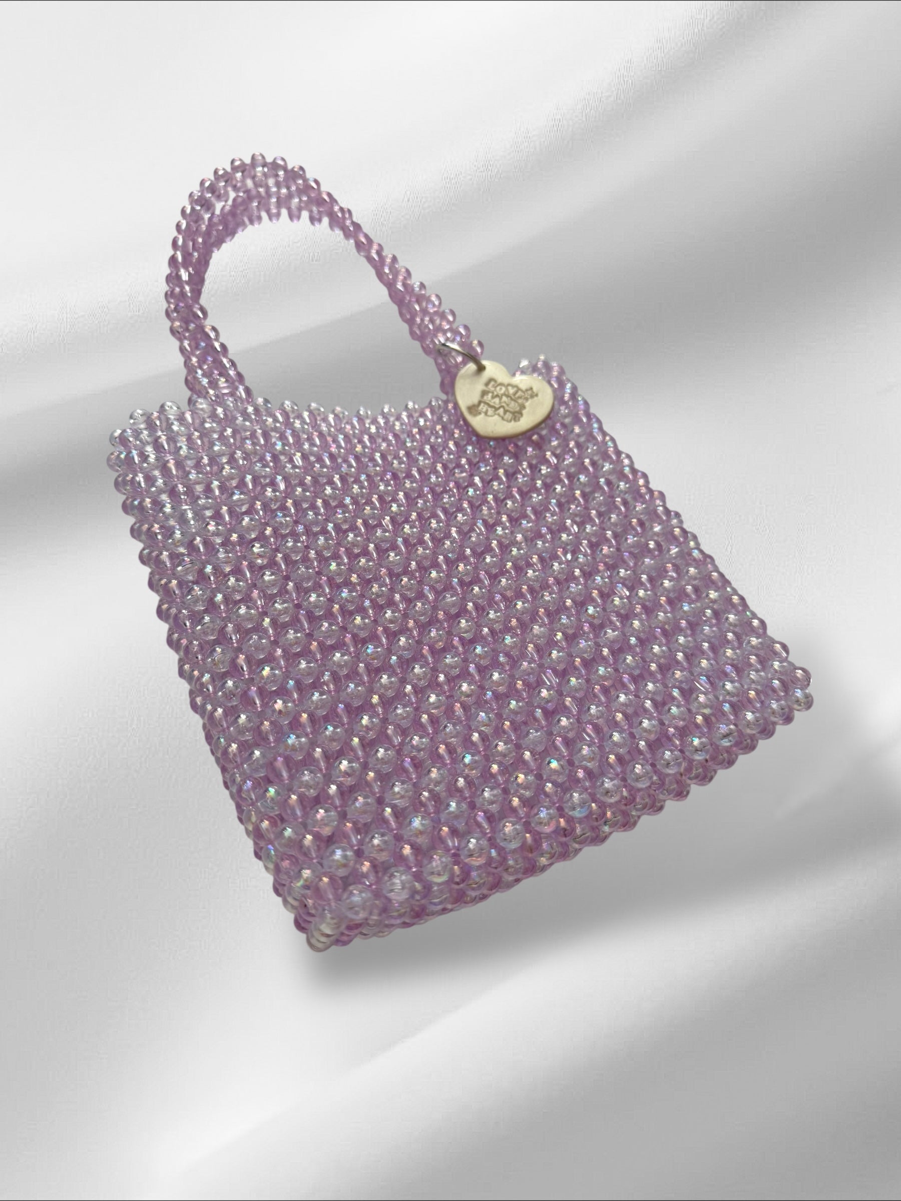 Purple beaded handbag with a white metallic clay tag on a light gray background
