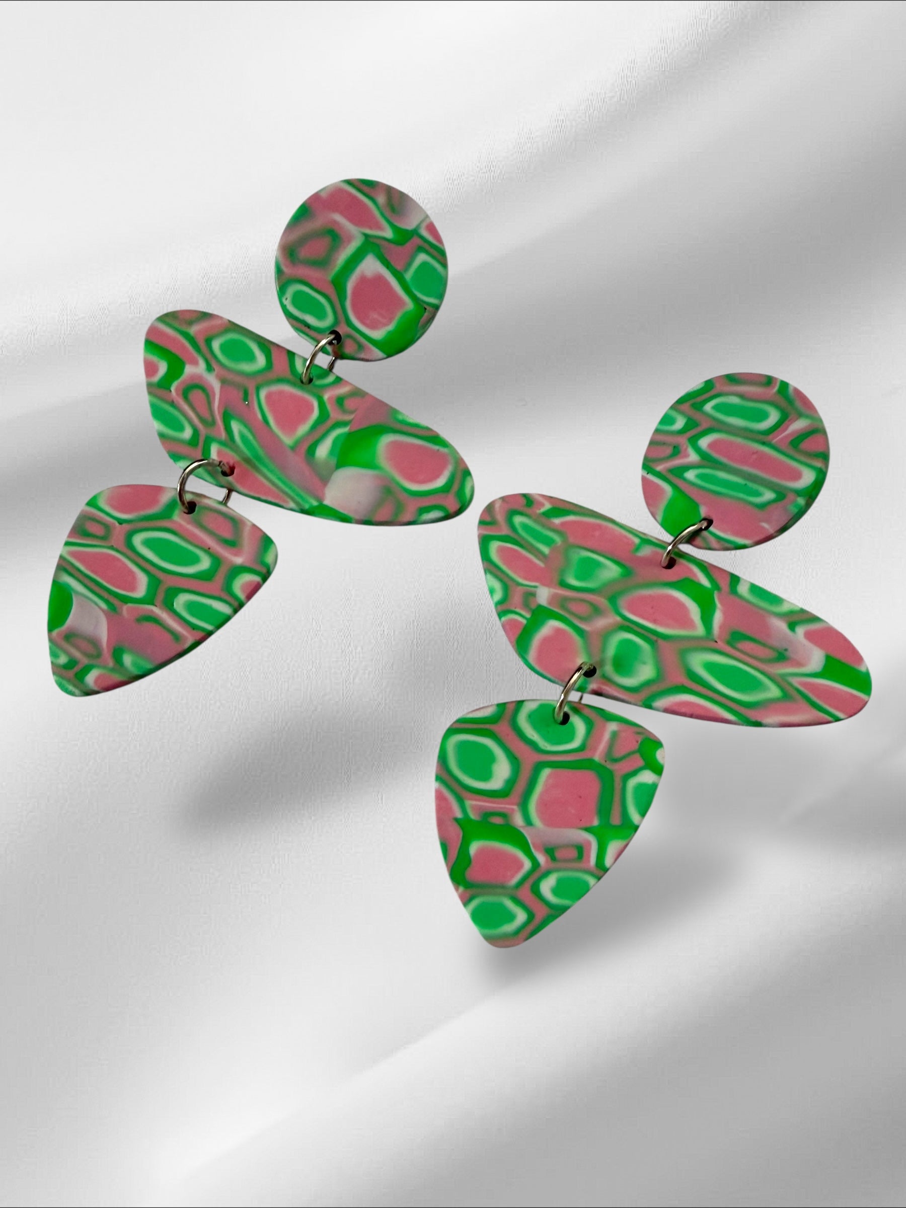 Pair of colorful earrings with pink and green pattern on a light gray background