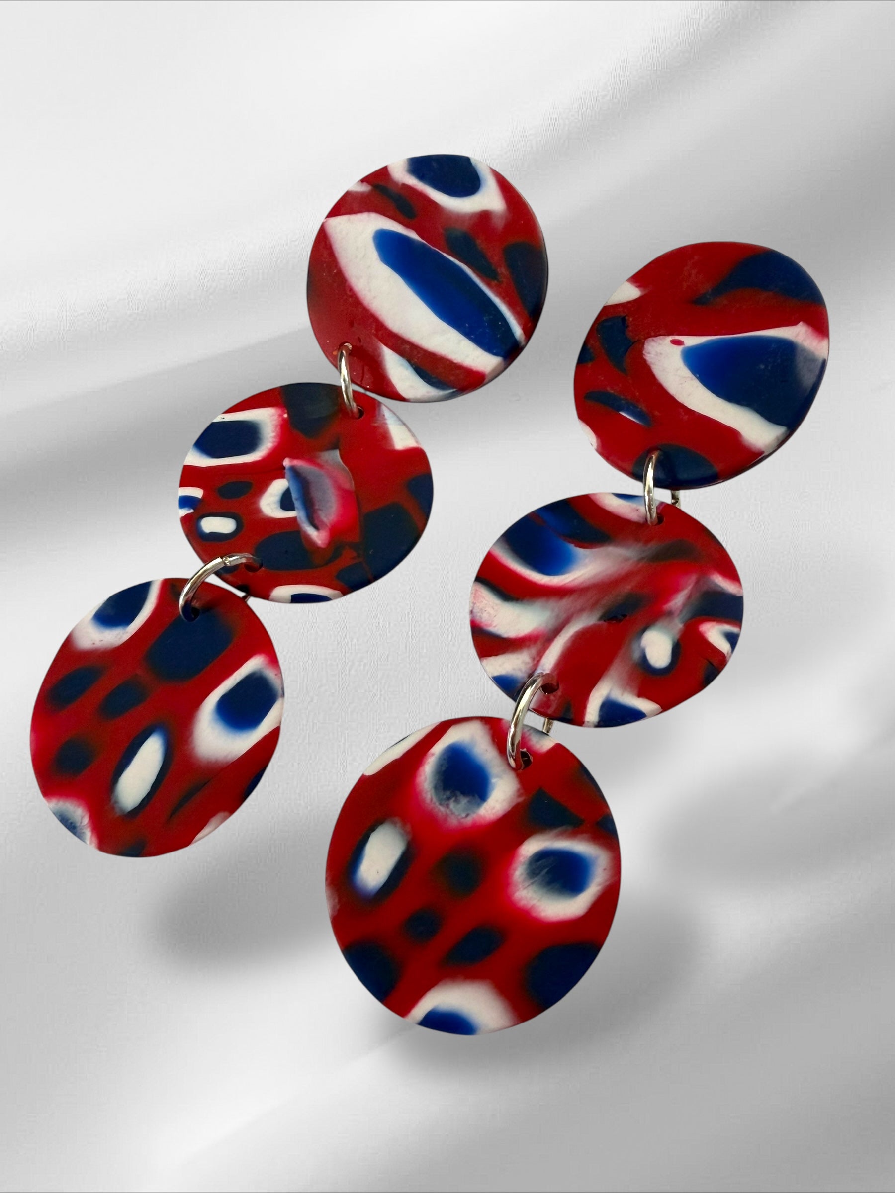Colorful circular earrings with red, blue, and white pattern on a light gray background