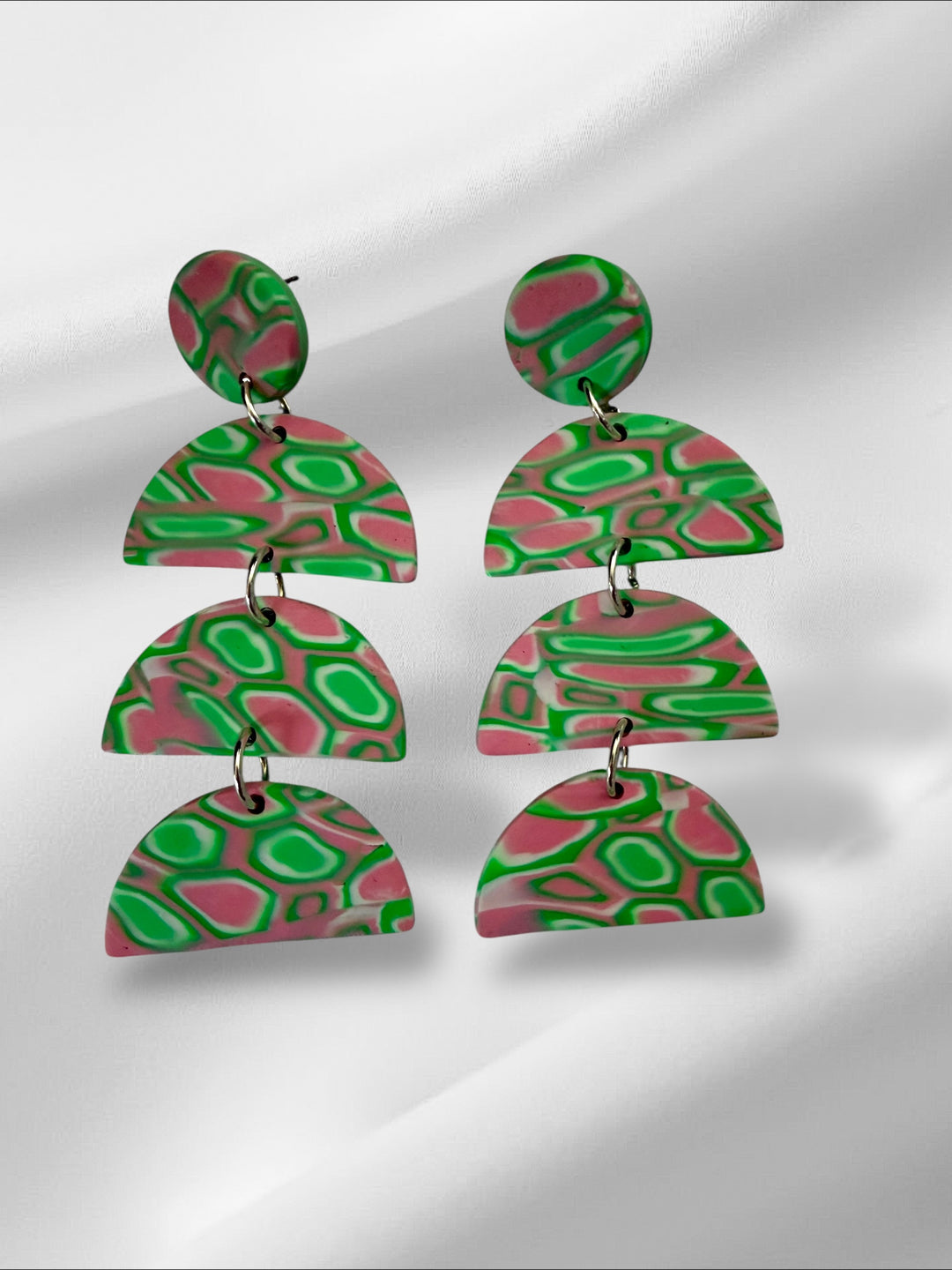 Pair of colorful earrings with a geometric design on a reflective surface.
