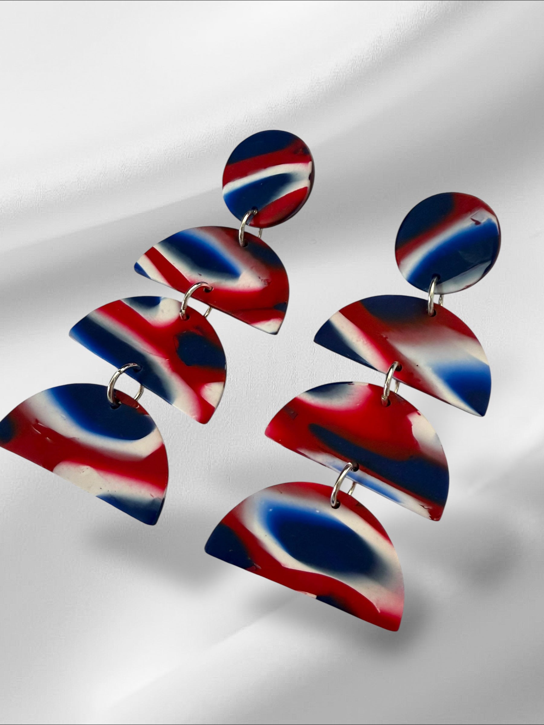 Pair of red, white, and blue abstract earrings on a reflective surface.