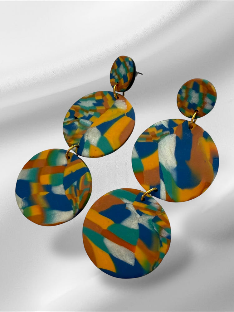 Colorful orange abstract patterned earrings on a reflective surface